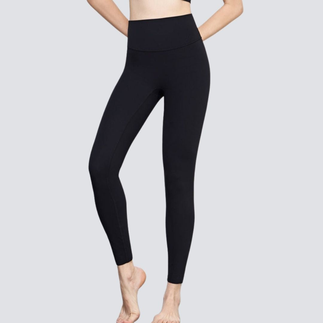 A pair of black leggings fit on a model, showcasing the product's snug fit and solid color.